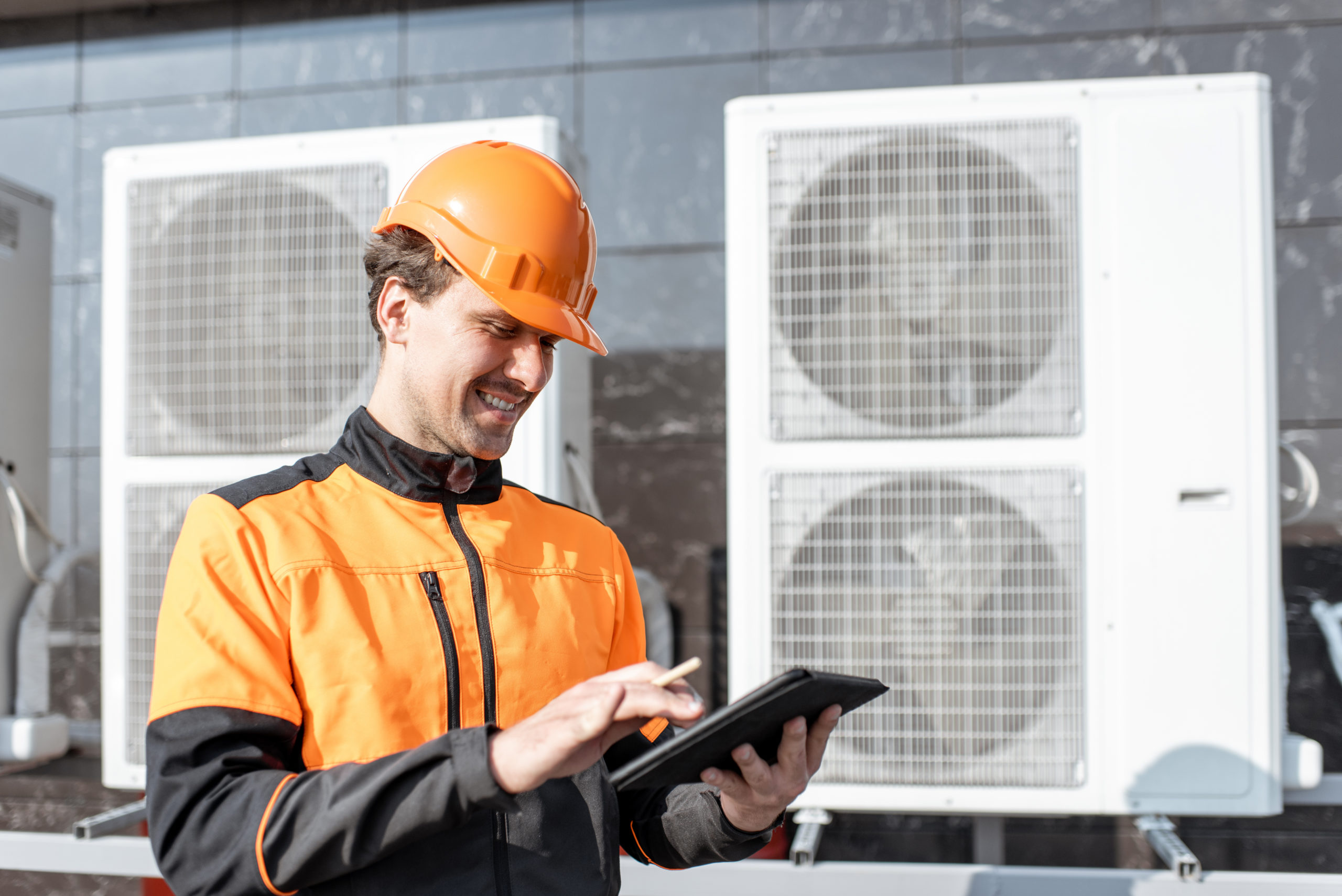 Professional workman in protective clothing adjusting the outdoor unit of the air conditioner or heat pump with digital tablet